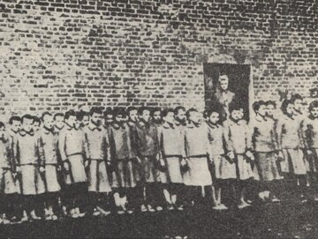 Dziewczęta na&nbsp;tle budynku podobozu dziewczęcego w&nbsp;obozie przy ul. Przemysłowej. W&nbsp;drzwiach stoi nadzorczyni Genowefa Pohl