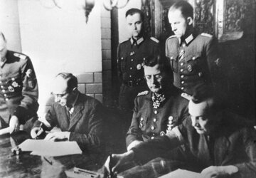 Podpisanie "Układu o&nbsp;zaprzestaniu działań wojennych w&nbsp;Warszawie&rdquo;, kończącego Powstanie Warszawskie. Od&nbsp;lewej siedzą: płk Kazimierz Iranek-Osmecki &bdquo;Heller&rdquo;, SS-Obergrupenf&uuml;hrer Erich von dem Bach-Zelewski, ppłk Zygmunt Dobrowolski. Ożar&oacute;w, 3.10.1944
