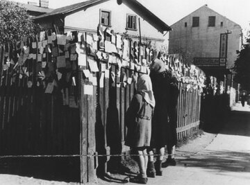 Fragment ogrodzenia  nieopodal zachodniej bramy obozu  z&nbsp;przypiętymi kartkami napisanymi przez warszawiak&oacute;w