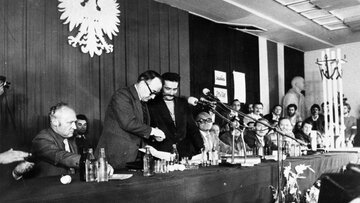 Wicepremier i&nbsp;przewodniczący Komisji Rządowej Mieczysław Jagielski (2L stoi) i&nbsp;przewodniczący Międzyzakładowego Komitetu Strajkowego Lech Wałęsa (3L stoi) podpisują (w sali BHP) porozumienie kończące strajk w&nbsp;Stoczni Gdańskiej im.&nbsp;Lenina