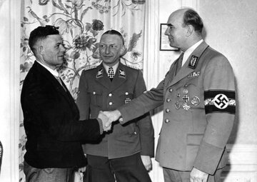 Heinz Reinefarth (w środku) wraz z&nbsp;Arthurem Greiserem wita milionowego Niemca przesiedlonego do&nbsp;Kraju Warty ze&nbsp;wschodniej Europy w&nbsp;ramach niemieckiej akcji przesiedleńczej Heim ins Reich &ndash; marzec 1944