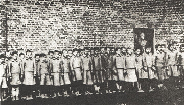Dziewczęta na&nbsp;tle budynku niemieckiego obozu dla&nbsp;dzieci w&nbsp;Łodzi, około 1943 rok