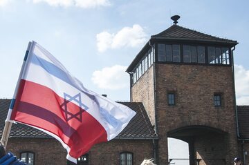 Flagi Polski i Izraela przed bramą do niemieckiego obozu koncentracyjnego Auschwitz