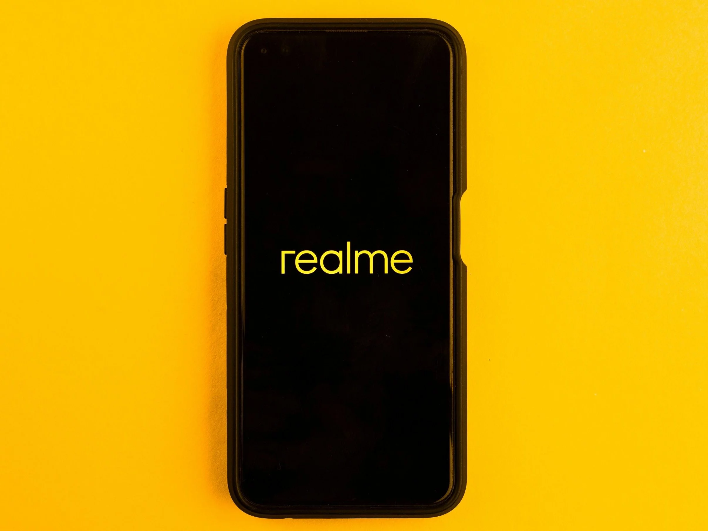 In this photo illustration the Realme logo seen displayed on a smartphone and on the background