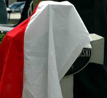 Polska flaga przykrywa krzyż na nagrobku, zdjęcie ilustracyjne