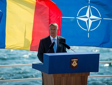 Prezydent Rumunii Klaus Iohannis na tle flag Rumunii i NATO