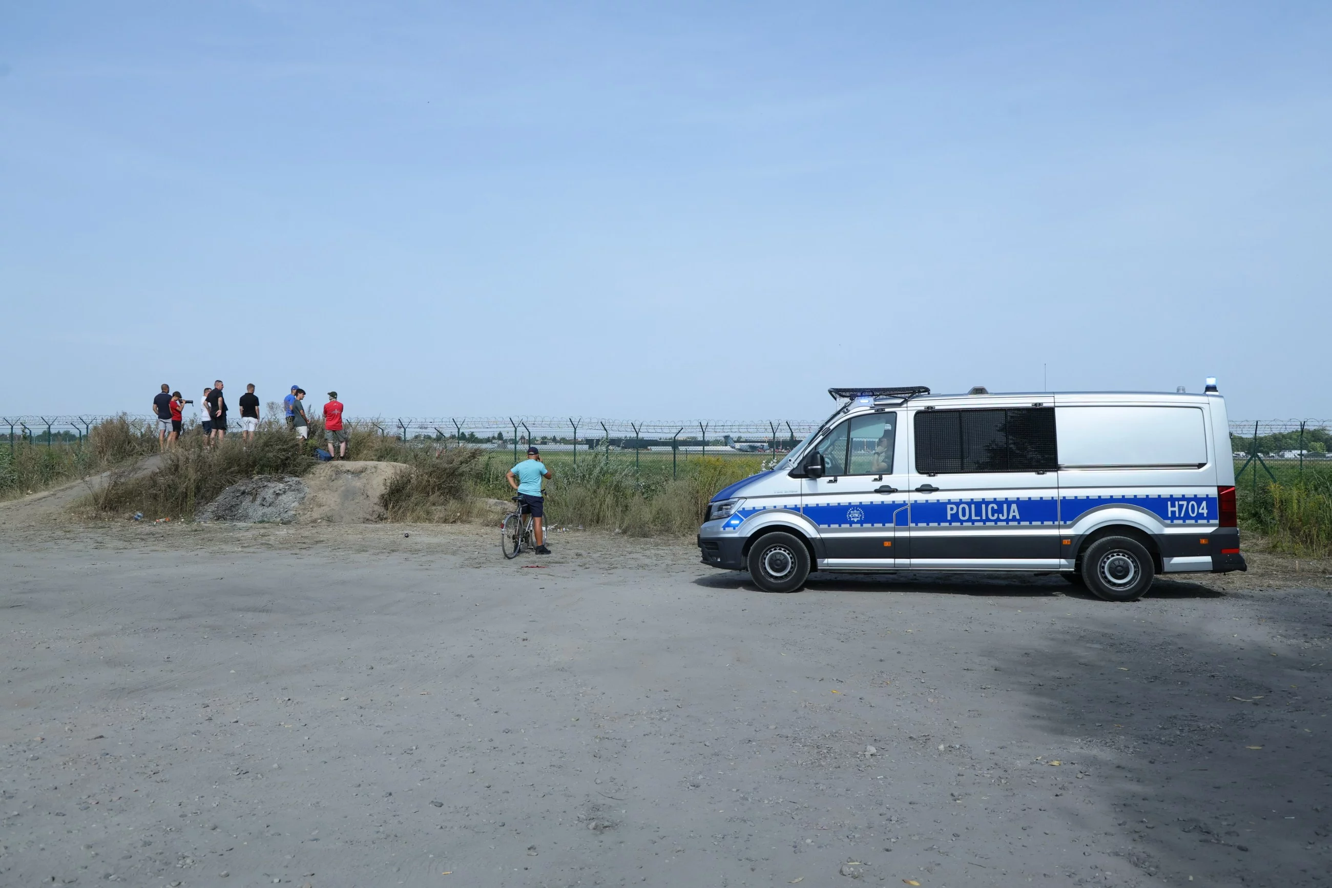 Policja obok zgromadzenia osób obserwujących pracę służb w miejscu katastrofy F-16 na terenie 42. Bazy Lotnictwa Szkolnego w Radomiu