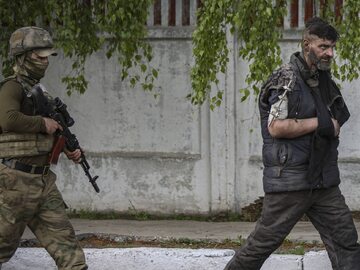 Rosyjski żołnierz eskortuje ukraińskiego wojskowego, ewakuowanego z zakładów Azowstal w Mariupolu