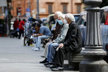 Starsi panowie w maseczkach ochronnych siedzący na ławce w Rzymie, zdjęcie ilustracyjne