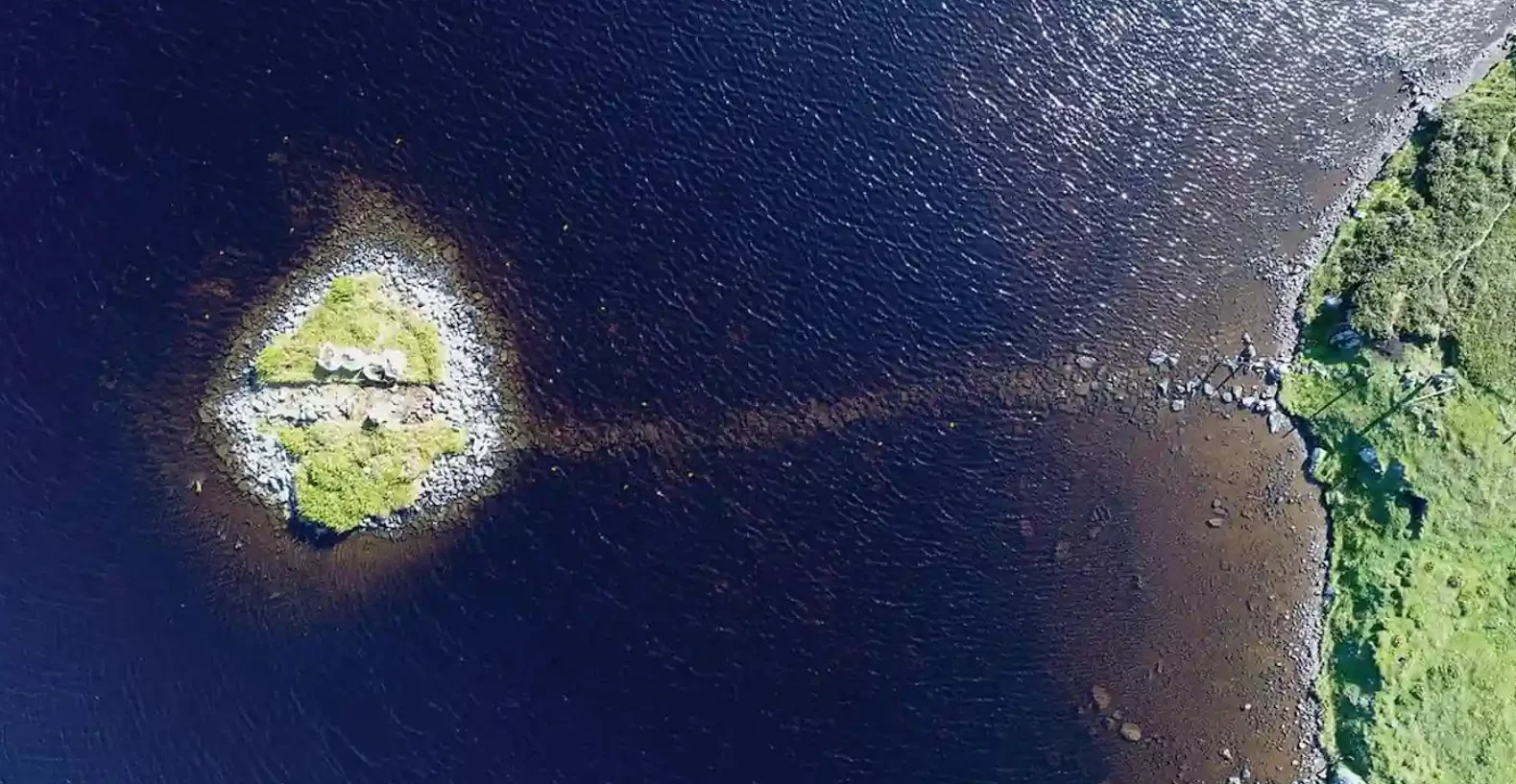 Crannog, czyli sztuczna wyspa na jeziorze Loch Bhorgastail, Szkocja. Na zdjęciu z góry widać groble łączącą wyspę z wodą. Grobla niegdsyś znajdowała się nad wodą